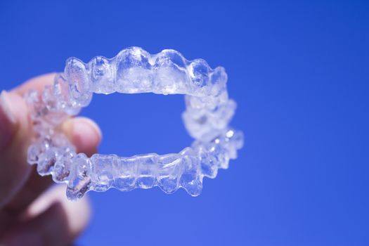 Invisible dental orthodontics held by woman hand on blue background