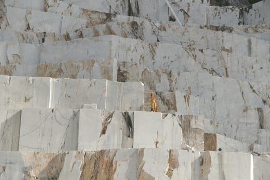 Carrara, Tuscany, Italy. About 09/2019. White Carrara marble quarry in Tuscany. Mountains of the Apuan Alps, blue sky and a mechanical excavator.
