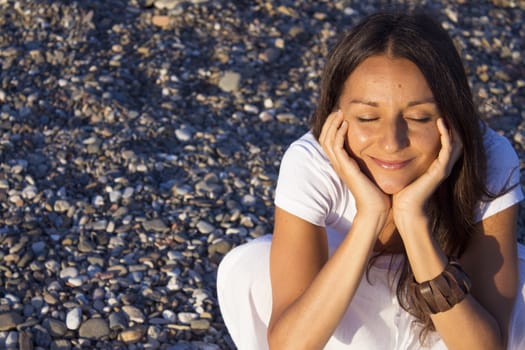 Woman sitting on stones with hands on the pensive face. Positive expression