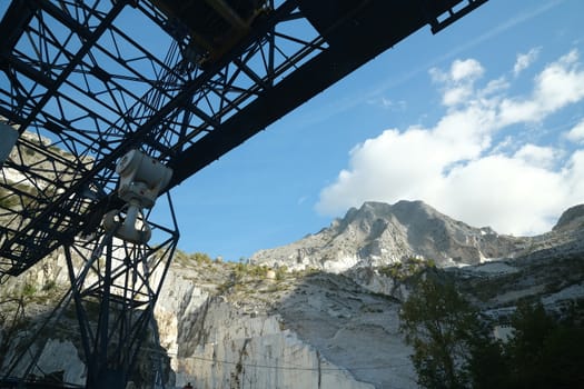 Panoramic view of the Apuan Alps from a quarry of white Carrara marble. A large overhead crane used to move marble blocks.