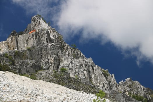 White Carrara marble quarry in the Apuan Alps. A mountain peak near Colonnata with blue sky and clouds.