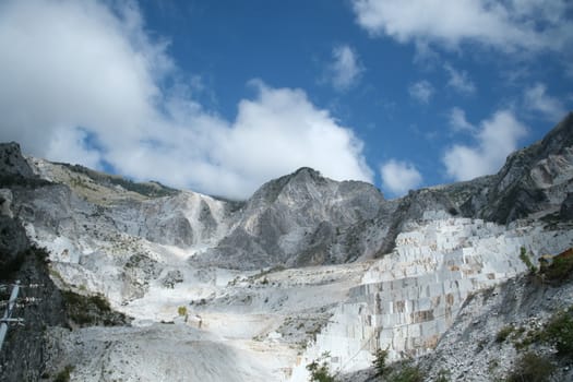 Panorama of a white Carrara marble quarry in Tuscany. Mountains of the Apuan Alps, blue sky and cloud.