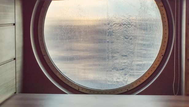 Round porthole of a sea cruise ship with water jets outside. Concept of sea travel.