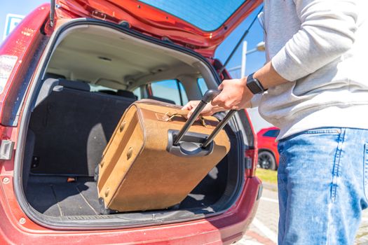 A young man puts luggage in the trunk of a car.