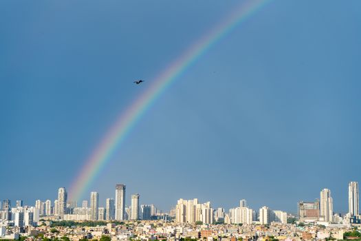 Aerial cityscape shot of buildings in gurgaon delhi noida with a rainbow behind them on a monsoon day. Shows the natural phenomenon in Jun 2020 where a double rainbow was seen in the indian capital