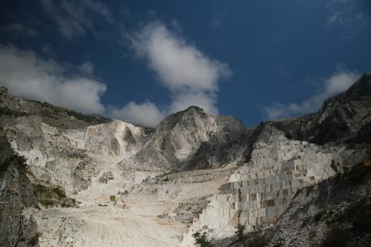 Panorama of a white Carrara marble quarry in Tuscany. Mountains of the Apuan Alps, blue sky and cloud.
