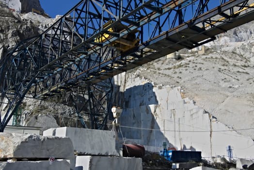 In a marble deposit on the Carrara mountains, an overhead crane is used to move the white marble blocks.