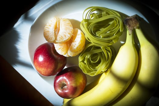 Plate with bananas, apples, tangerine and spinach pasta without cooking
