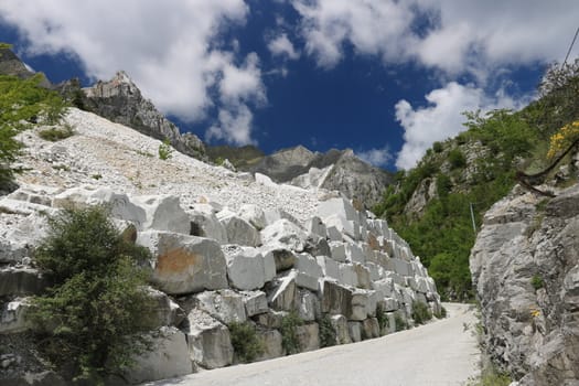White Carrara marble quarries near Colonnata. A steep street with white marble blocks and the mountains of the Apuan Alps.