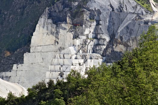 White Carrara marble quarry in the Apuan Alps. A mountain peak near Colonnata with blue sky and clouds.