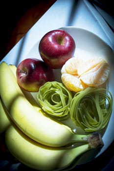 Plate with bananas, apples, tangerine and spinach pasta without cooking