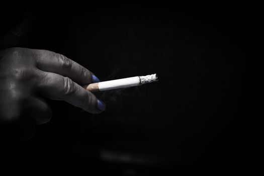 Womans hand holding lit cigarette. Dark background