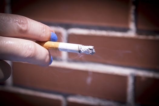 Womans hand holding lit cigarette. Dark background