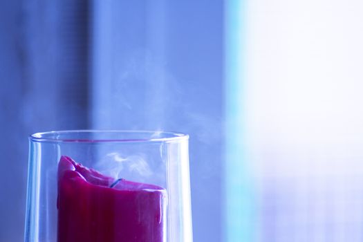 Red candle inside a clear glass vase just blown out. No people