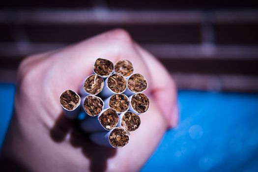 Womans hand holding cigarettes roll on blue background
