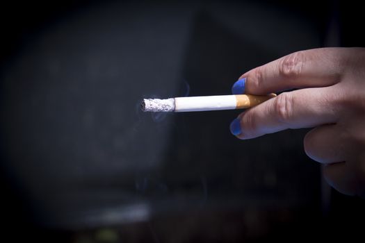 Womans hand holding lit cigarette. Dark background
