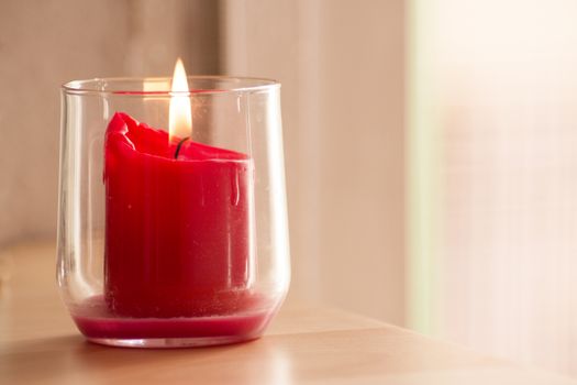 Burning red candle inside a clear glass vase. No people