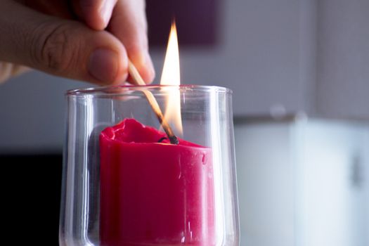 Fingers of man lighting a red candle inside a transparent glass vase with a match