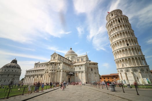 Pisa, Tuscany, Italy. 06/21/2019.  Piazza dei miracoli of Pisa. Travelers admire architecture. Cathedral, leaning tower of the Tuscan city. Blue sky with clouds.