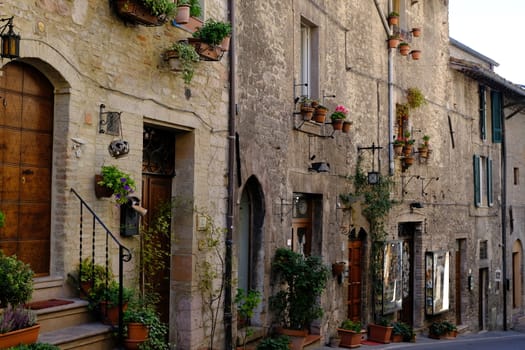 Assisi, Umbria, Italy. About october 2019. Street of the city of Assisi with typical old stone and brick houses. Facades, doors and windows are decorated with flower pot plants