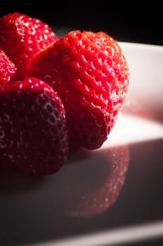 Ripe strawberries on a white plate and dark background. No people