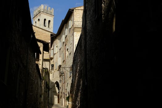 Alley of the city of Assisi with bell tower and stone houses. Narrow street of the city with the walls of the stone houses. Deserted road.