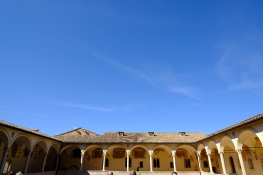 Assisi, Umbria, Italy. About october 2019. Cloister with columns and arches at the Basilica of San Francesco in Assisi. In the center of the courtyard there is a well in beige stone.