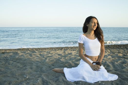 Girl dressed in white sitting on the beach sand. Sunset