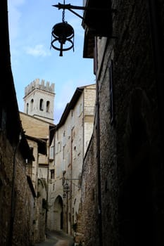 Alley of the city of Assisi with bell tower and stone houses. Narrow street of the city with the walls of the stone houses. Deserted road.