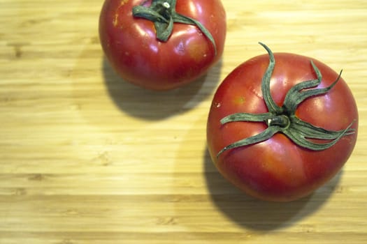 Two red ripe tomatoes on wooden cutting board. No people