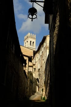 Alley of the city of Assisi with bell tower and stone houses. Narrow street of the city with the walls of the stone houses. Deserted road.