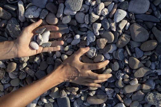 Woman hands touching stones on the beach. Grey stones