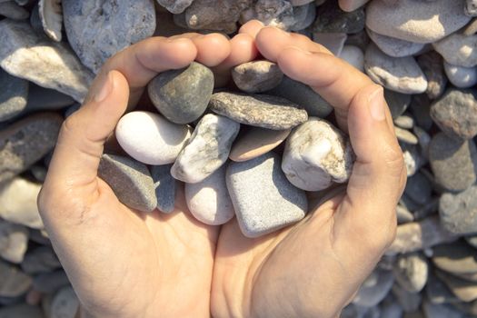 Woman hands touching stones on the beach. Grey stones