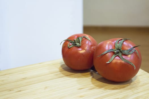 Two red ripe tomatoes on wooden cutting board. No people