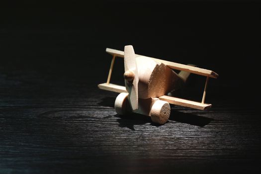 Travel concept. Small wooden airplane under beam of light on dark background