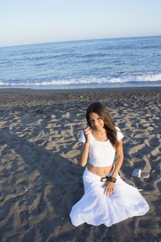 Girl dressed in white sitting on the beach sand. Sunset