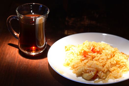 White plate with pilaf near cup of tea on wooden table