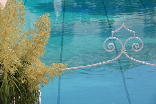 Swimming pool with blue water. Dracaena flower and white wrought iron ornament.