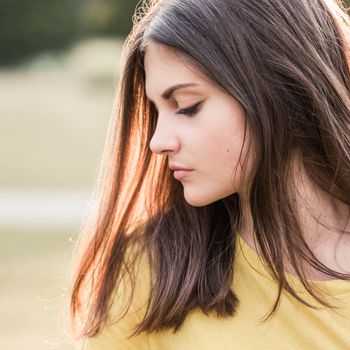 Profile portrait of a teenage girl with long hair on a nature background