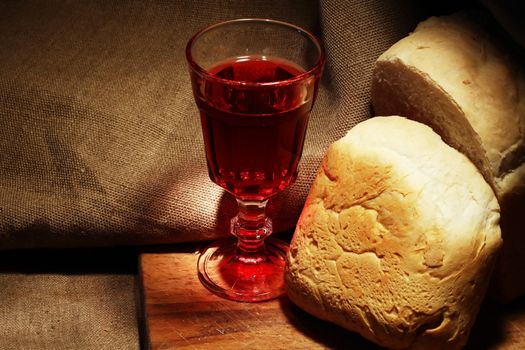 Loaf of white bread near glass of red wine on canvas background
