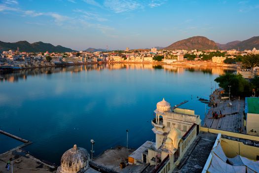 View of famous indian hinduism pilgrimage town sacred holy hindu religious city Pushkar amongst hills with Brahma mandir temple, lake and traditional Pushkar ghats at dusk sunset. Rajasthan, India