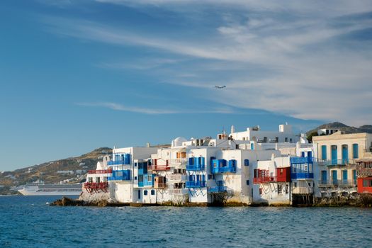 Sunset in Mykonos island, Greece with yachts in the harbor and colorful waterfront houses of Little Venice romantic spot on sunset and cruise ship and plane. Mykonos townd, Greece