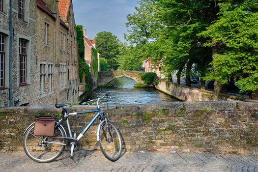 Typical Belgian scenic cityscape Europe tourism and bicycle transport concept - bicycle on a bridge near canal and old house. Bruges (Brugge), Belgium