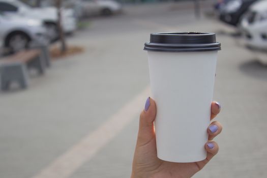 Breakfast and coffee theme: a woman's hand holding a white paper coffee Cup with a black plastic lid. Coffee advertising