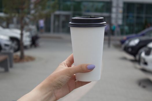 Breakfast and coffee theme: a woman's hand holding a white paper coffee Cup with a black plastic lid. Coffee advertising