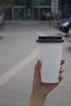 Breakfast and coffee theme: a woman's hand holding a white paper coffee Cup with a black plastic lid. Coffee advertising