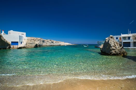 Greece scenic island view - small harbor with fishing boats in crystal clear turquoise water, traditishional whitewashed house. MItakas village, Milos island, Greece.