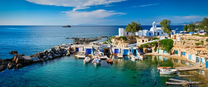 Panorama of typical Greece scenic island view - small harbor with fishing boats in crystal clear turquoise water, traditional white houses church. Mandrakia village, Milos island, Greece.