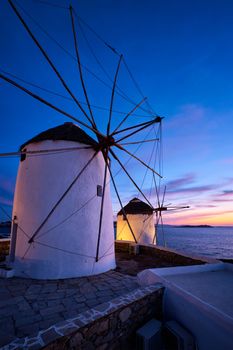 Scenic view of famous Mykonos Chora town windmills. Traditional greek windmills on Mykonos island illuminated in the evening, Cyclades, Greece. Walking with steadycam.