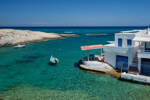 Greece scenic island view - small harbor with fishing boats in crystal clear turquoise water, traditional whitewashed house. Mitakas village, Milos island, Greece.